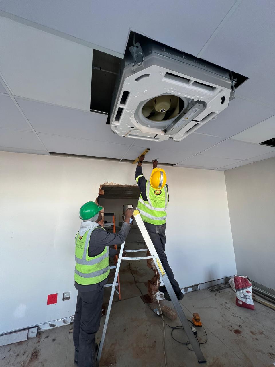 TTS technicians working at height, levelling a Hisense ceiling cassette unit into place before final fit-out